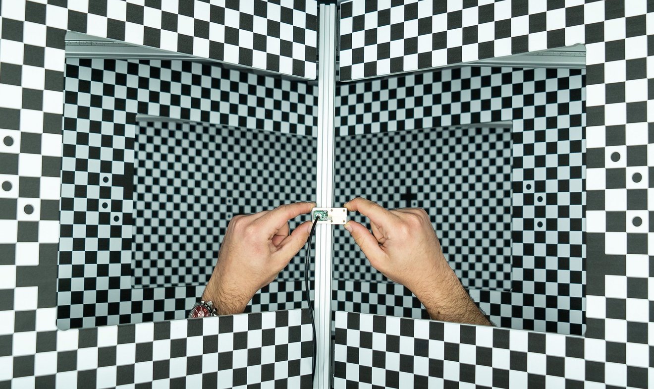 Zwei Hände halten eine Miniatur-Kamera vor Schachbrettmuster
