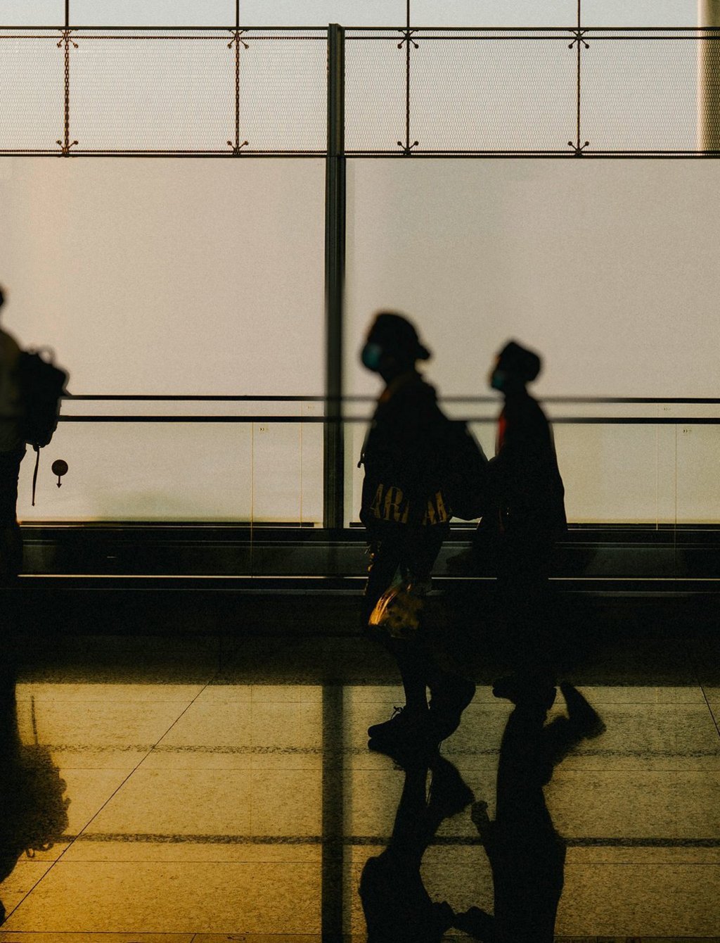 Foto von drei Menschen im Gegenlicht mit Rucksack in einer verglasten Halle, die in eine Richtung laufen.