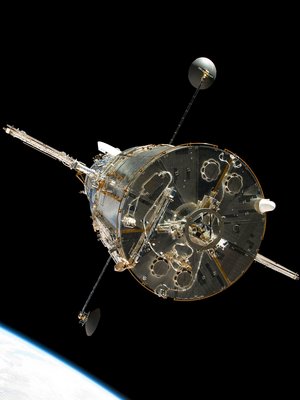 Aufnahme des Teleskopes "Hubble", das im Weltall schwebt. Am linken Bildrand ist ein Planet zu erkennen. Das Gefährt steht frei im dunkeln Raum. Es ist von unten aufgenommen, an den Seiten sind Antennen zu sehen.