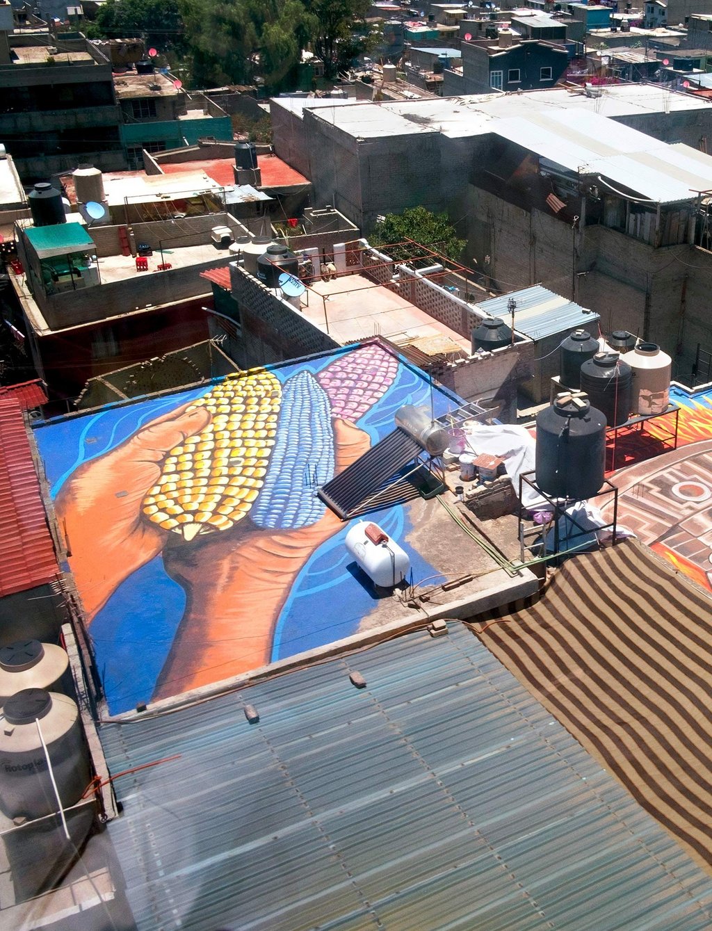 Aerial view from the gondola of colorful painted roofs of the workers' district of Cuautepec. Two hands are painted on one of the roofs holding three corn cobs.