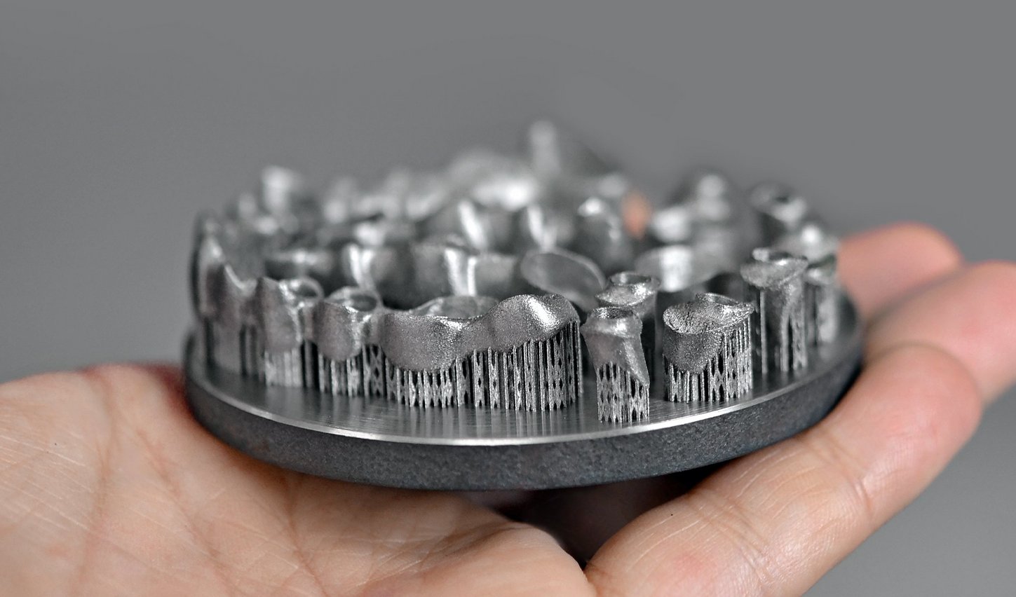 Eine Hand hält ein metallenes Gebiss aus dem 3D-Drucker