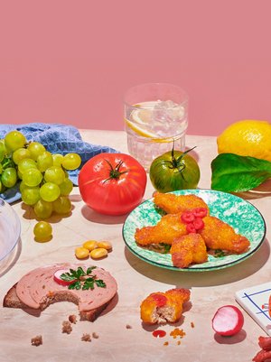 Photo of food on pink marble against an old pink background. Natural and processed foods side by side. Fruits, vegetables and vegan sausages are decoratively arranged, next to it is a blue kitchen towel.