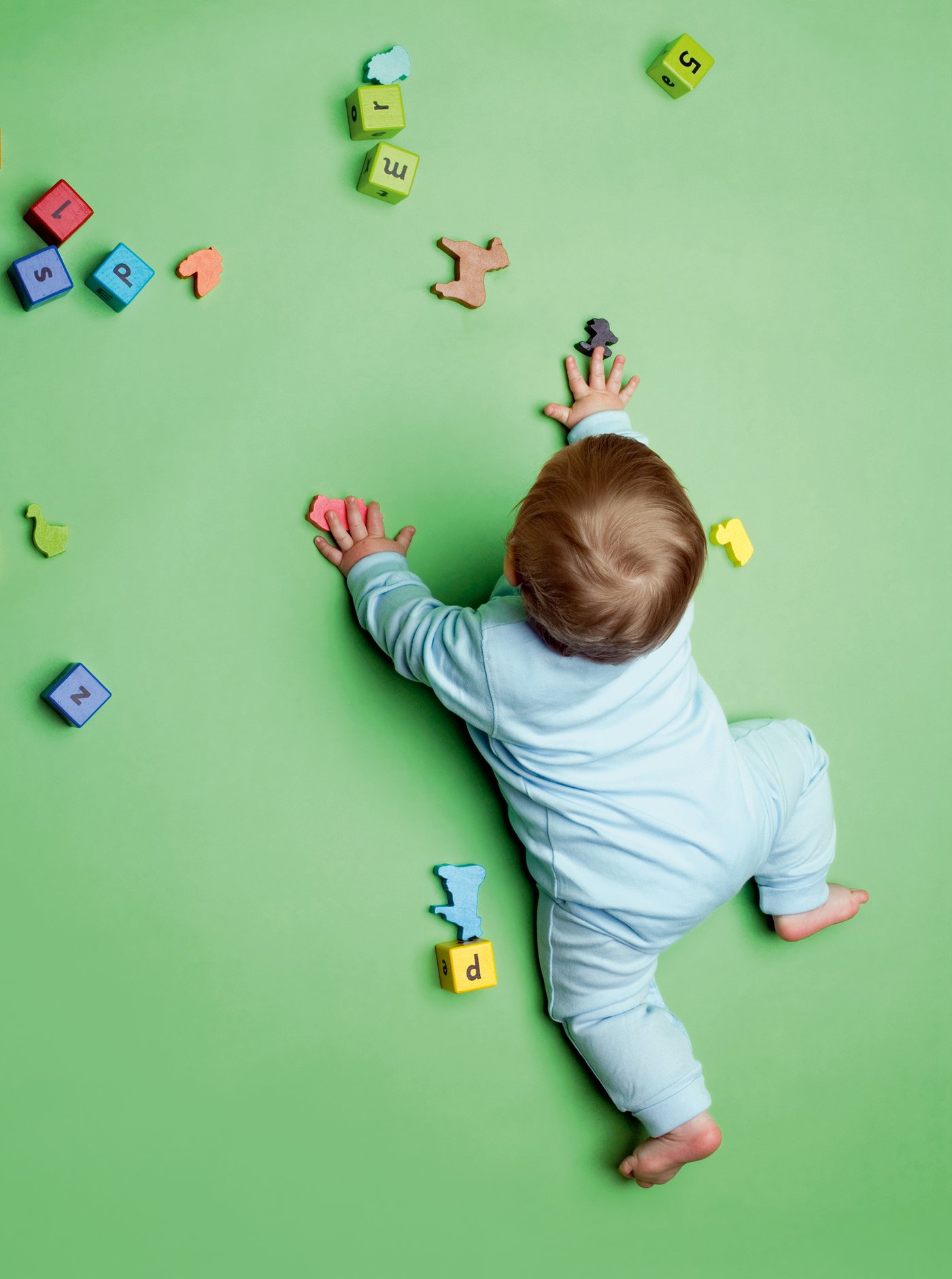 Bild von Baby auf Boden, das  von bunten Spielzeugklötzen und Tieren aus Holz umgeben ist.