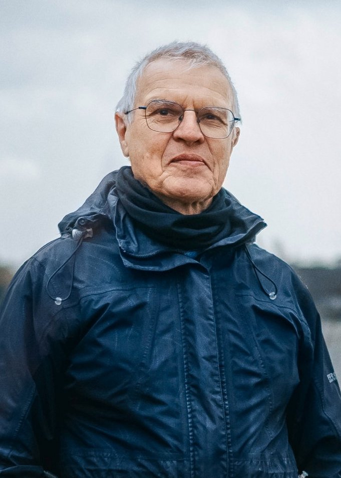 Portrait photo of Johannes Frech looking into the camera from glasses and a black rain jacket.