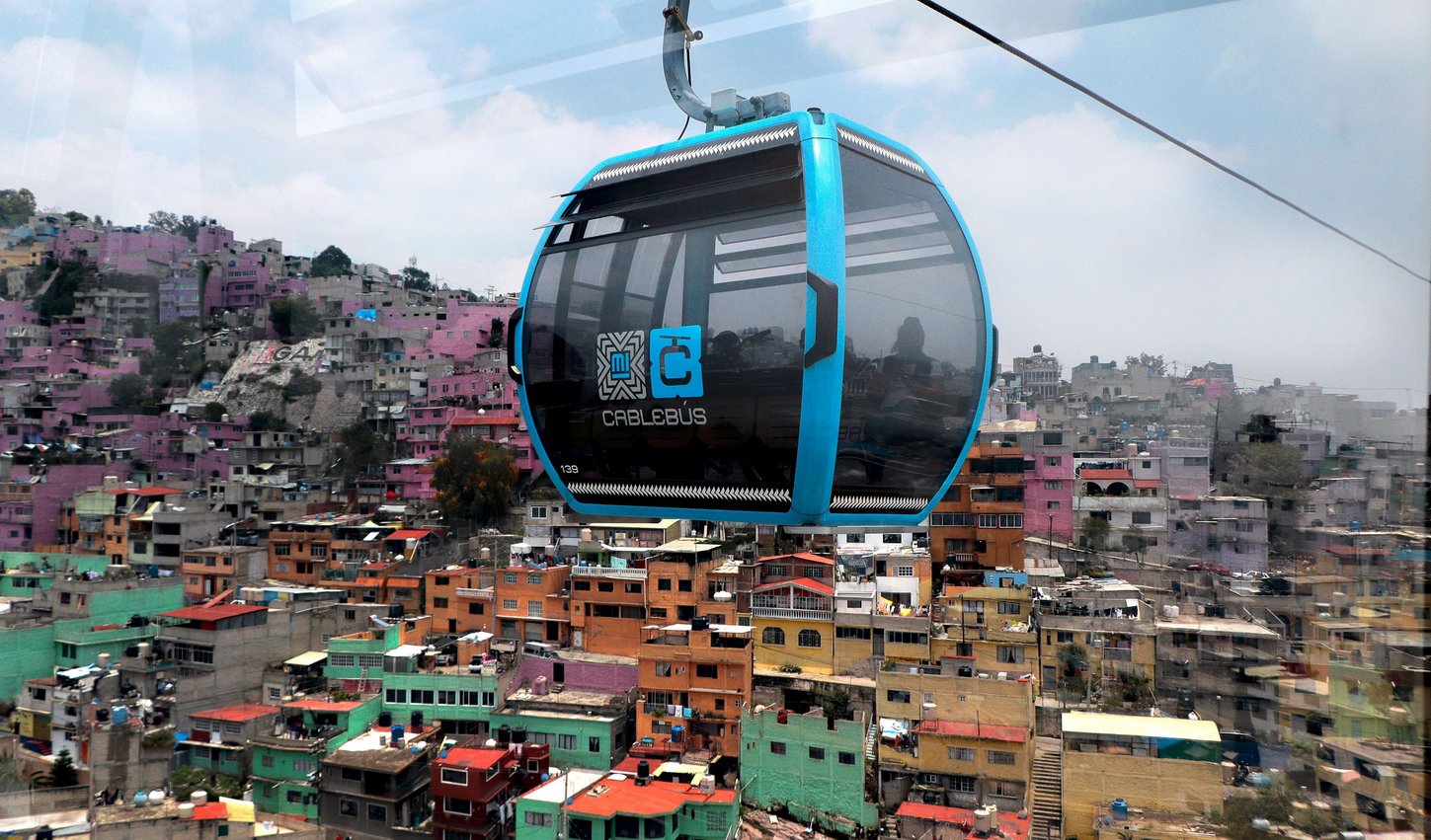 Photo of gondolas of the ropeway, in the background the Mexico City panorama of rooftops and mountains.