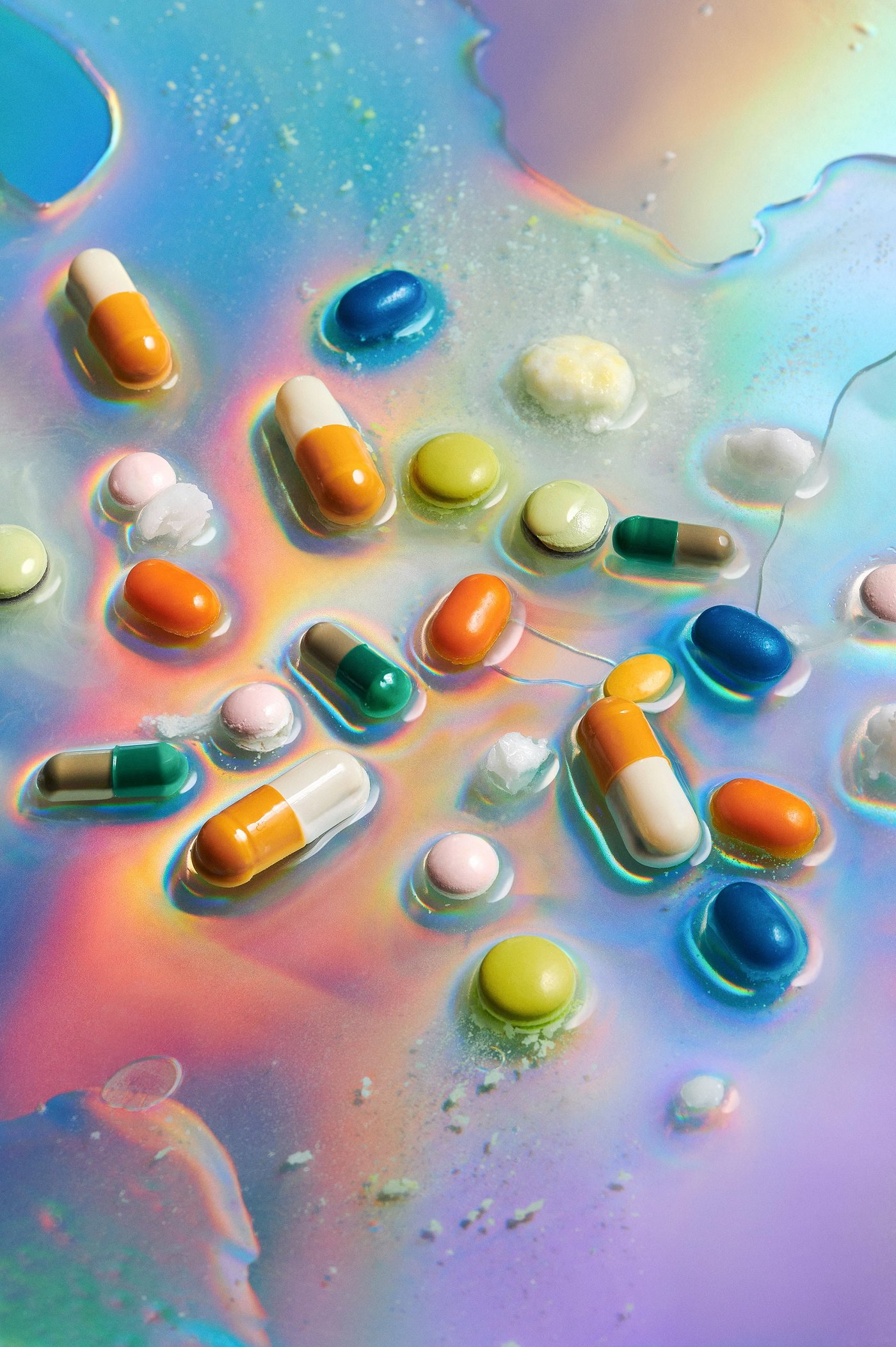 Photo of pills and tablets of different colors lying in transparent liquid. Some are in a state of dissolution. The liquid shimmers colorfully and fluoresces. 