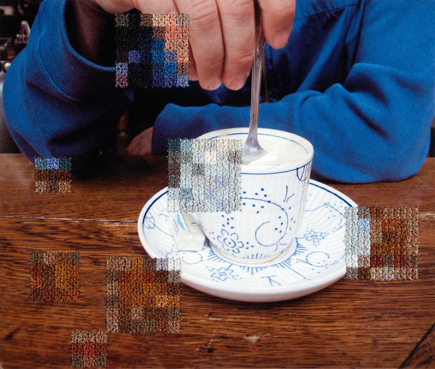 Bild einer weißen Kaffeetasse mit blauem Muster. Eine Hand rührt mit einem Löffel den Schaum um. Teile des Bildes sind mit einem Strickmuster verpixelt.